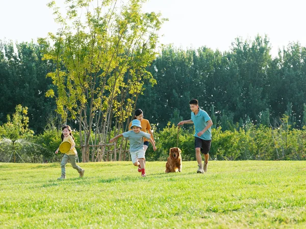 Familia feliz de cuatro y perro mascota jugando en el parque — Foto de Stock