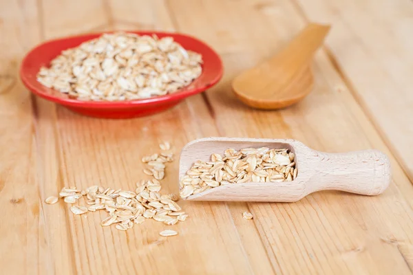 red dish and wood spoon with oats flakes pile on wood