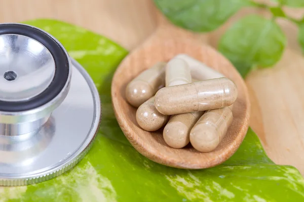 Capsules of herbs on spoon and stethoscope — Stock Photo, Image