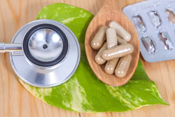 Capsules of herbs on spoon and stethoscope — Stock Photo, Image