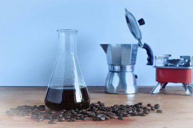 Tahta sehpanın üzerinde kahve çekirdeği ile laboratuvar tüpünde sıcak kahve demlemek..