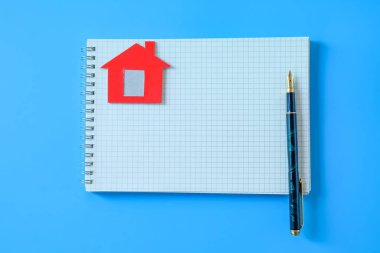 Renk arkaplanına küçük kırmızı ev ve defter.