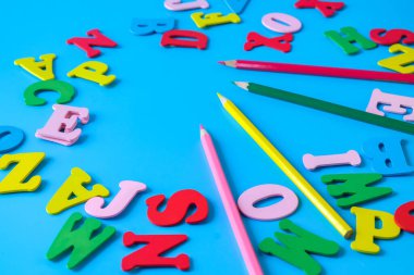 Çocuklar için alfabe harfleri ve renkli arka planda renk kalemleri.