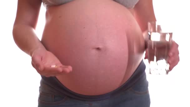 임신 한 여자는 물과 약을 한 컵씩 먹습니다. 하얀 배경 위에 있는 벨트 — 비디오