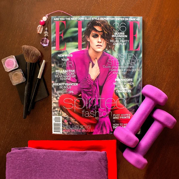 Mode tijdschrift Elle, januari februari Zuid-Afrikaanse edition met dieprode, violet kleren, make-up tools en halters op houten achtergrond. — Stockfoto