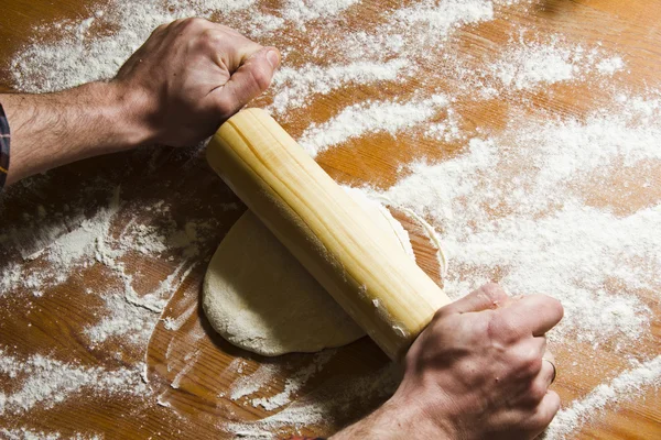 Hombre lanza pastelería en la mesa de la cocina de madera con rodillo . — Foto de Stock