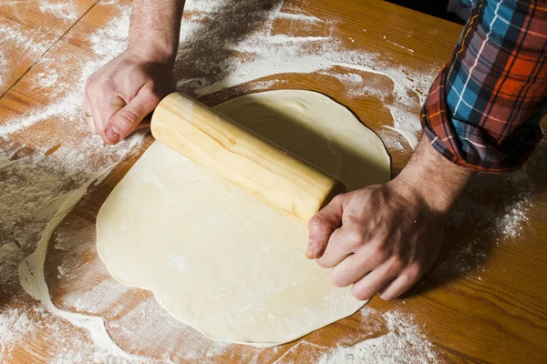 Hombre lanza pastelería en la mesa de la cocina de madera con rodillo . — Foto de Stock