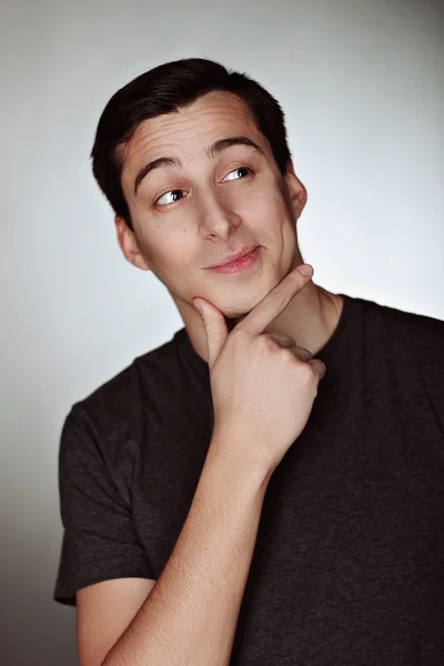 Profundo en el pensamiento exitoso joven guapo con camiseta sobre fondo gris . — Foto de Stock