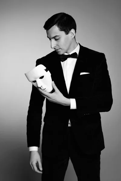 Diep in de gedachte succesvolle knappe jonge man in kostuum met witte masker. Zwart-wit beeld. — Stockfoto