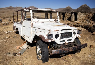 Kimliği belirsiz kırık terk edilmiş beyaz araba arka plan etnik Afrika rondavels terk edilmiş köyün yanındaki Sani geçmek, Lesotho.