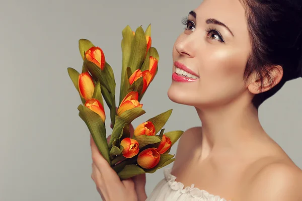 Spring beauty model studio schieten. Portret van lachende mooie vrouw met bloemen oranje geel tulpen op witte achtergrond. Mode verse make-up. Sensuele dieprode lippen. Tederheid. Romantische stijl. — Stockfoto