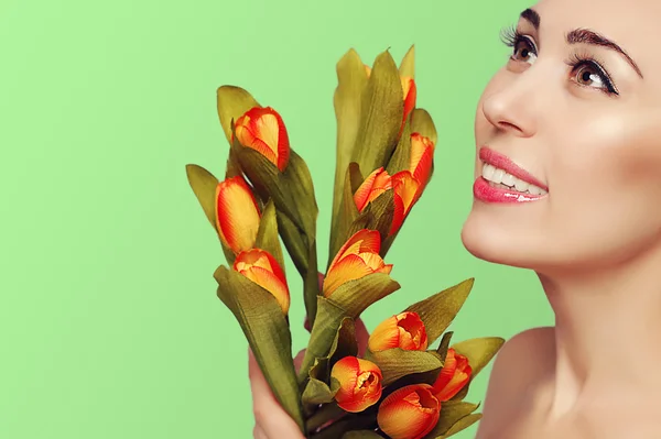 Spring beauty model studio shooting. Close-up portrait of smiling young woman brunette  with flowers orange tulips on green background. Fashion fresh makeup. Perfect skin. Tenderness. Romantic style. — Stock Photo, Image