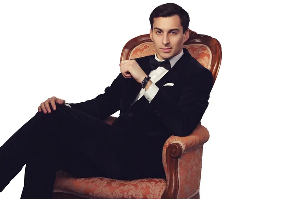 Selbstbewusster erfolgreicher junger, gutaussehender Geschäftsmann im eleganten Anzug mit Fliege sitzt auf einem Vintage-Sessel auf weißem Hintergrund. Männlichkeit. männliche Schönheit. Modelstudio gedreht. italienischer Stil. — Stockfoto