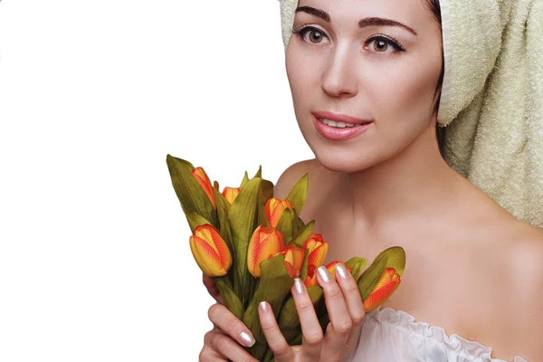 Joven mujer hermosa en turbante de toalla con flores de tulipanes sobre fondo blanco. Cuidado de la piel. Salón de spa. Belleza y salud. Piel perfecta transparente . — Foto de Stock