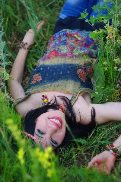 躺在鲜花和绿草的微笑美丽的年轻女子嬉皮。时装模特拍摄。波西米亚风格。波西米亚风别致。享受大自然。健康笑容. — 图库照片