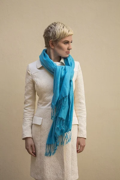 Stylish beautiful young woman blonde wearing blue scarf and white pattern coat isolated on beige background. Girl with short hair. Professional nude makeup. Fashion fresh make-up. Model shooting. Elegant style. — Stock Photo, Image