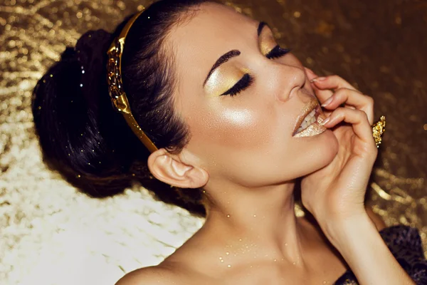 Junge schöne Frau Brünette mit Retro-Frisur, Reifen. Goldgrund. Modellschießen. Mädchen mit Gold Mode Make-up. Luxus. Eleganz. Sexualität. Sinnlichkeit. — Stockfoto