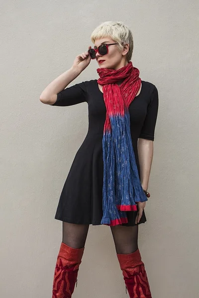 Stylish young beautiful woman blonde in black little dress, red scarf and sunglasses isolated on grey background. Girl with short hair. Fashion haircut. Trendy hairstyle. Model shot. — Stock Photo, Image