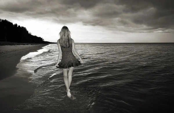 Yalnız kız deniz ve fırtınalı gökyüzü ile bir plajda yürüyüş