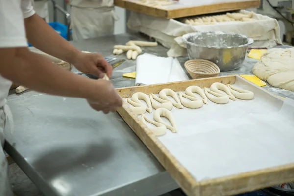 Panettieri che producono pretzel freschi sulla tavola ricoperta di pasta — Foto Stock