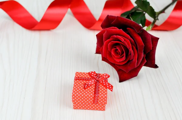 Red rose and gift box on a wooden table. Valentine's Day.