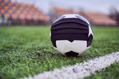 Boş bir stadyumda siyah maskeli futbol topu. Boş stadyum koltuklarının arka planı. Futbol yarışmalarının iptali