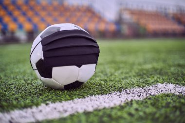 Boş bir stadyumda siyah maskeli futbol topu. Boş stadyum koltuklarının arka planı. Futbol yarışmalarının iptali