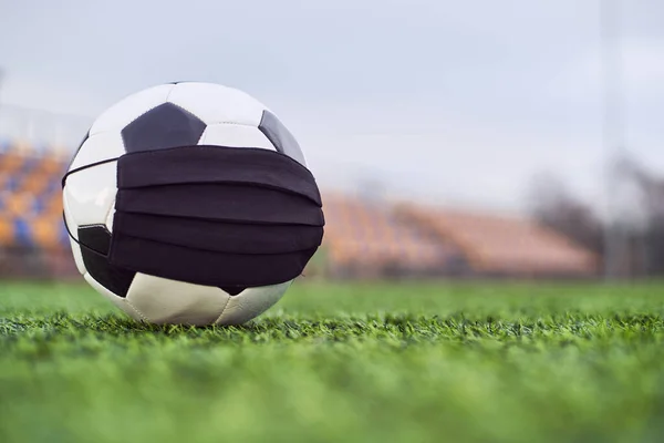 Boş bir stadyumda siyah maskeli futbol topu. Boş stadyum koltuklarının arka planı. Futbol yarışmalarının iptali