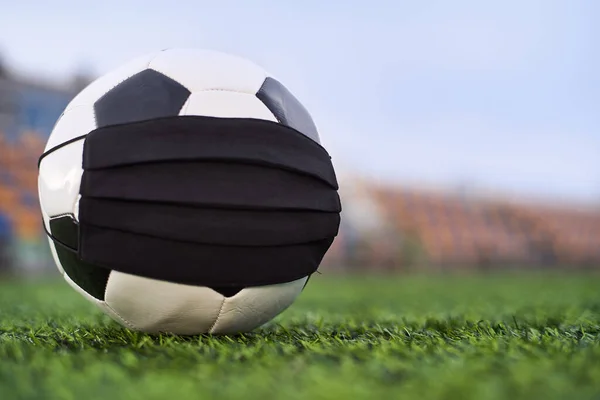 Boş bir stadyumda siyah maskeli futbol topu. Boş stadyum koltuklarının arka planı. Futbol yarışmalarının iptali