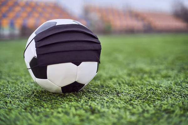 Boş bir stadyumda siyah maskeli futbol topu. Boş stadyum koltuklarının arka planı. Futbol yarışmalarının iptali