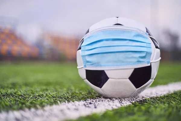 Medikal Maskeli Siyah ve Beyaz Futbol Balosu Stadyumun Çimlerinde Yatar. Arka planda Stadyumun Boş Koltukları var. Karantina zamanında futbol müsabakaları. COVID-19 Konsepti