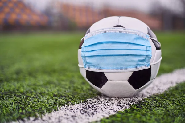 Medikal Maskeli Siyah ve Beyaz Futbol Balosu Stadyumun Çimlerinde Yatar. Arka planda Stadyumun Boş Koltukları var. Karantina zamanında futbol müsabakaları. COVID-19 Konsepti