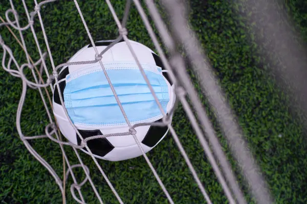 Medikal Maskeli Siyah ve Beyaz Futbol Balosu Stadyumun Çimlerinde Yatar. Arka planda Stadyumun Boş Koltukları var. Karantina zamanında futbol müsabakaları. COVID-19 Konsepti