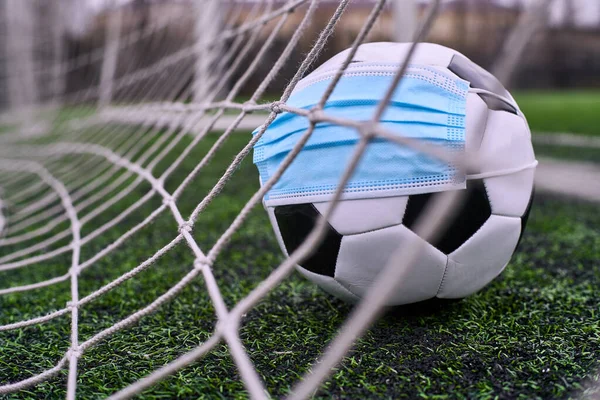 Futbol topu tıbbi maskeli Gol Ağı 'nda. Boş Stadyum. Futbol Yarışmalarının İptal Edilmesi