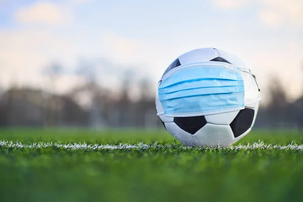 Medikal Maskeli Siyah ve Beyaz Futbol Balosu Stadyumun Çimlerinde Yatar. Arka plan Boş Stadyum ve Gökyüzü. Karantina zamanında futbol müsabakaları. COVID-19 Konsepti