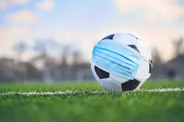 Medikal Maskeli Siyah ve Beyaz Futbol Balosu Stadyumun Çimlerinde Yatar. Arka plan Boş Stadyum ve Gökyüzü. Karantina zamanında futbol müsabakaları. COVID-19 Konsepti