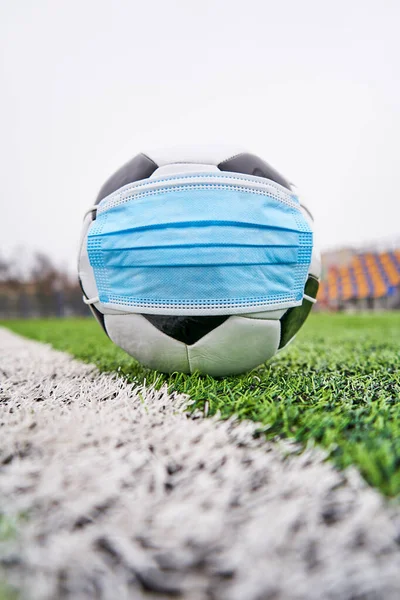 Boş stadyumda futbol topu. Koronavirüsten korunmak için tıbbi maskeli futbol topu, insanlar olmadan plastik koltuklardan korunmak için. Dikey fotoğraf