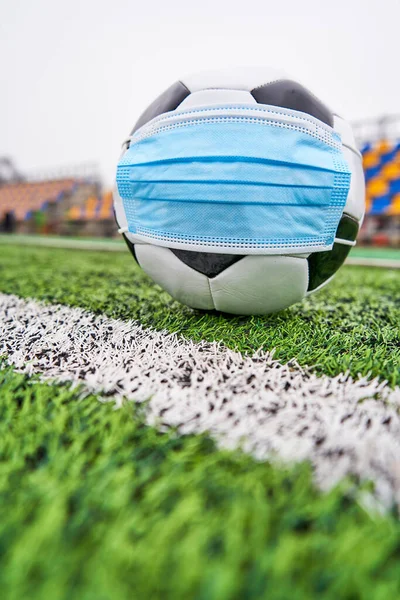 Boş stadyumda futbol topu. Koronavirüsten korunmak için tıbbi maskeli futbol topu, insanlar olmadan plastik koltuklardan korunmak için. Dikey fotoğraf