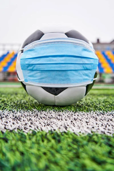 Boş stadyumda futbol topu. Koronavirüsten korunmak için tıbbi maskeli futbol topu, insanlar olmadan plastik koltuklardan korunmak için. Dikey fotoğraf