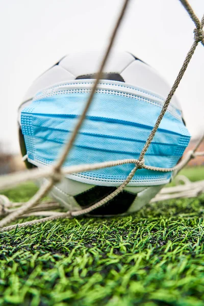 Futbol topu boş bir stadyumda tıbbi maske takıyor. Top futbol kalesinde. Coronavirus koruması. Salgın nedeniyle futbol müsabakalarının iptali. Dikey Fotoğraf