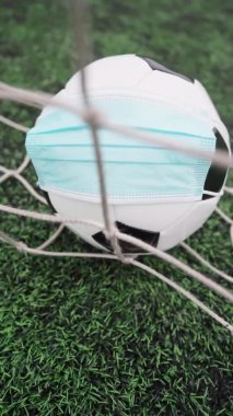 Futbol topu stadyum çimlerinde tıbbi maske takıyor. Futbol Gol Ağı İçinde Siyah ve Beyaz Top. Dikey Video