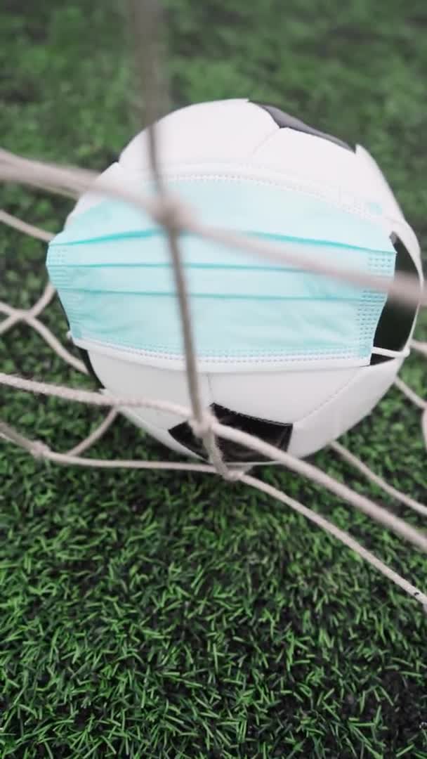 球技場草の上に医療マスクを着用サッカーボール サッカーのゴールネットで黒と白のボール 垂直ビデオ — ストック動画