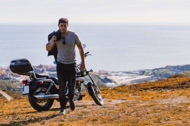 Deri ceketli bisikletçi motosikletten uzaklaşıyor.