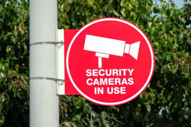 Güvenlik kameraları direğe bağlı kırmızı daire işareti kullanıyor. Bulanık ağaçlar arka plan.