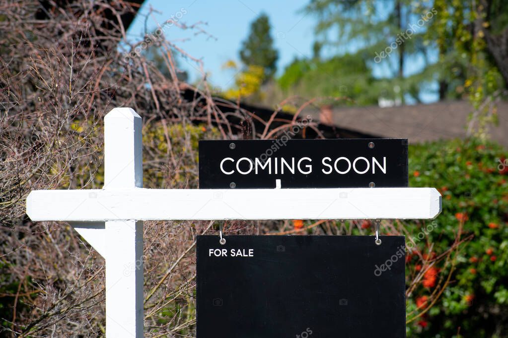Coming Soon sign near a house for sale in a residential neighborhood. Green trees background.