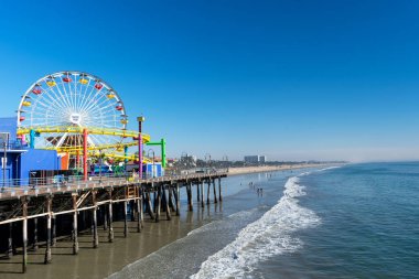 Ünlü Santa Monica İskelesi 'ndeki lunaparkta Batı hız treni ve dönme dolap. Kum plajına düşen okyanus dalgaları - Santa Monica, California, ABD - 2020