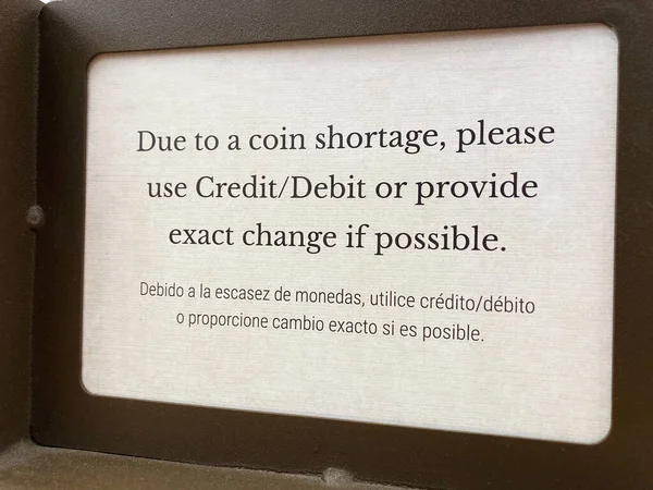 Bilingual sign in English and Spanish language: Due to a coin shortage, please use credit or debit card or provide the exact change