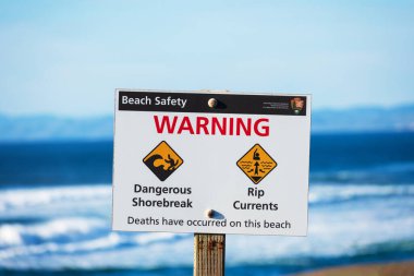 Sahil güvenlik uyarısı, ziyaretçilere tehlikeli kıyı kırıntıları ve akıntılar hakkında bilgi veriyor. Arka planda bulanık okyanus dalgaları - Point Reyes, California, ABD - 2021