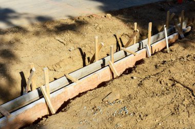 Ahşap işlemeli beton kaldırım inşaatı. Tahta, tahta kazıkları yere çakılarak dik konuma getirilir. Kazılmış alan