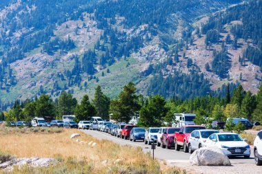 Cars of National Park visitors parked along the road during peak season near Jenny Lake. Scenic mountain background. - Grand Teton National Park, Wyoming, USA - 2020 clipart